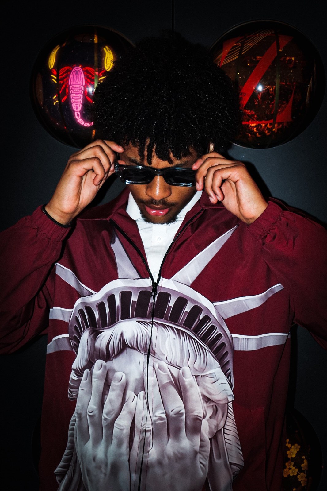 Michael Taylor, founder of Topnxtch Visualz, in a maroon jacket and sunglasses, photographed against a black wall with glowing displays